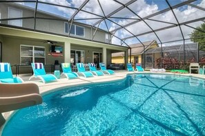Una piscina interior con agua cristalina y azul, rodeada de sillones de descanso y una zona cubierta con techo de cristal.