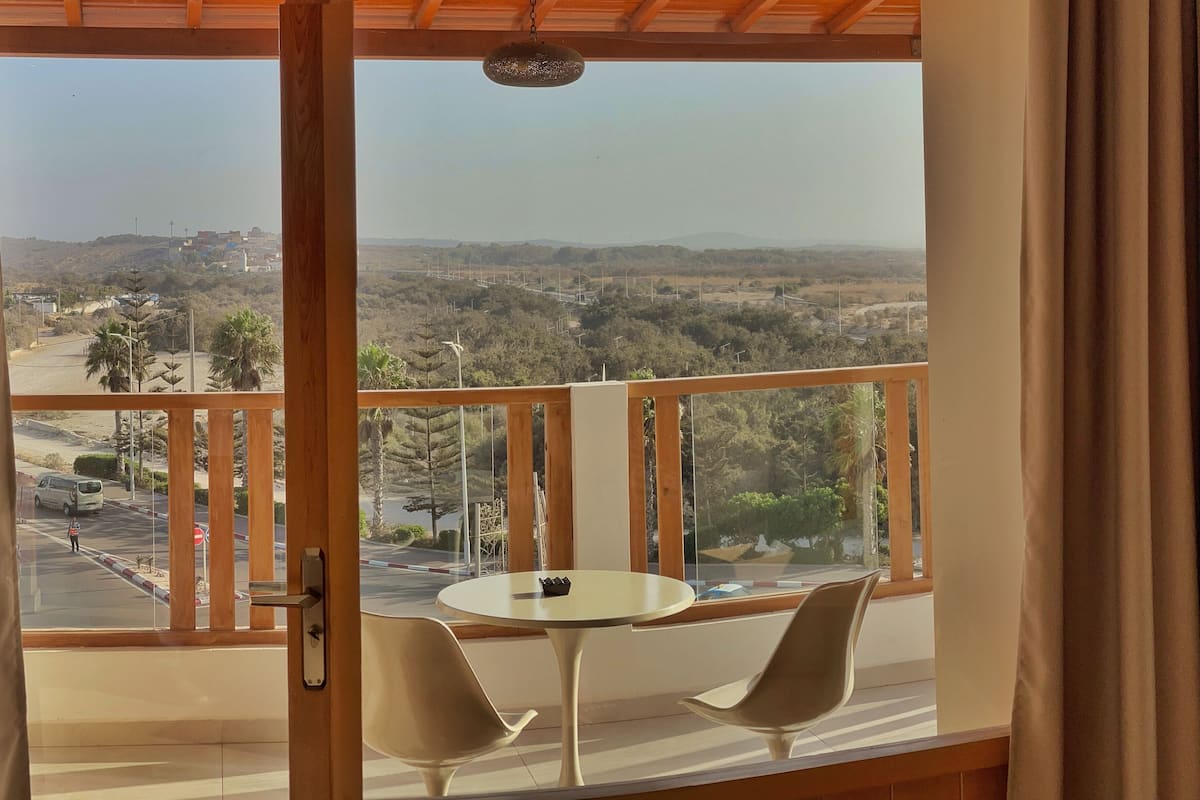 Een balkon met een tafel en twee stoelen, met uitzicht op een stadsgezicht met gebouwen en groen.