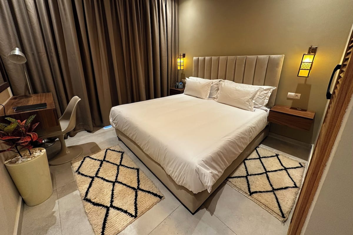 Een moderne hotelkamer met een groot bed, twee nachtkastjes, een bureau met stoel en een kamerplant.
