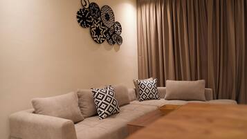 Uma sala de estar moderna com um sofá bege, almofadas estampadas, uma mesa de centro de madeira e um objeto decorativo fixado na parede.