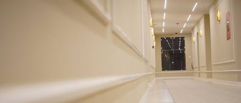 A hotel corridor with a long, straight path, light-colored walls, and ceiling lights.