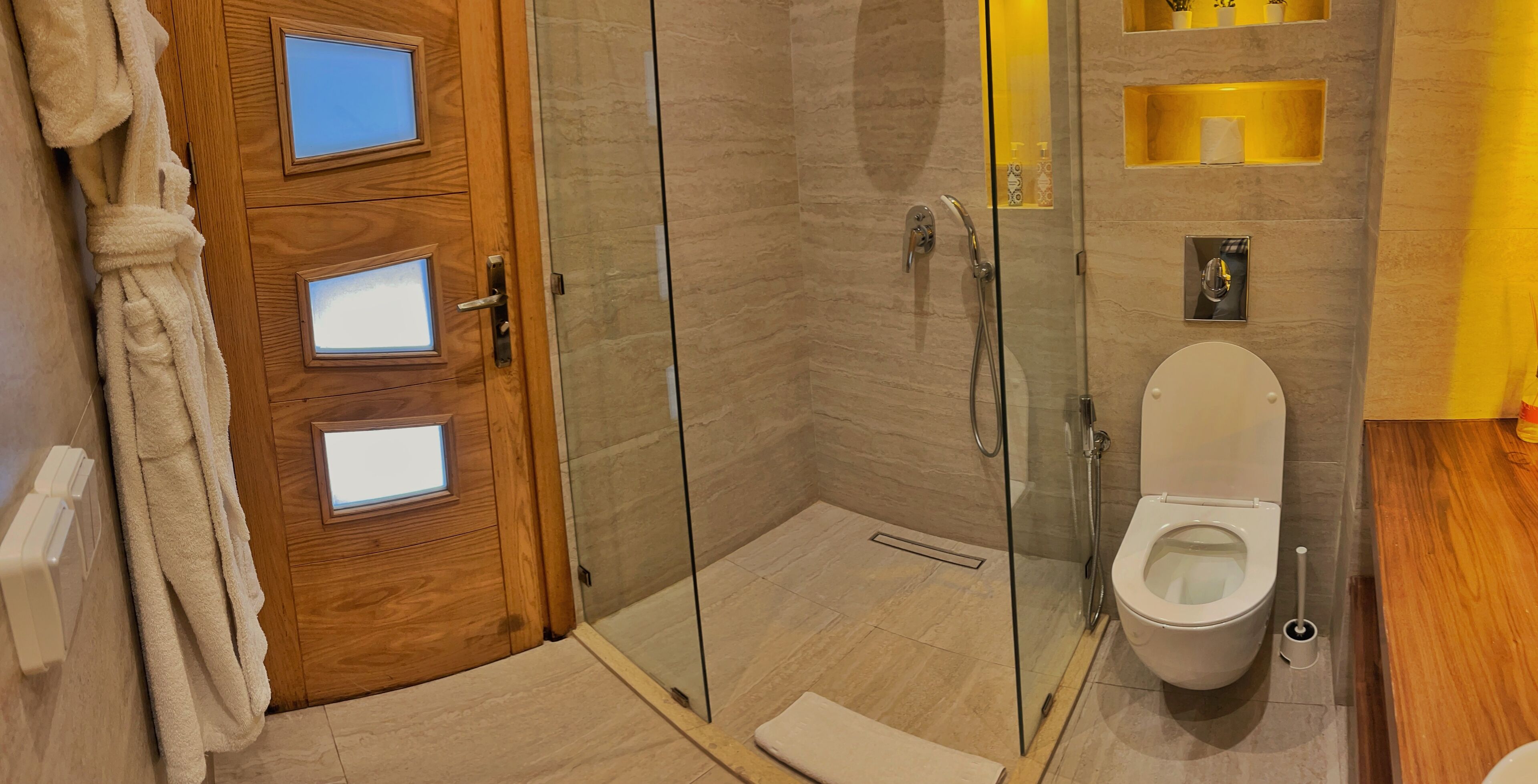 Un bagno moderno con doccia vetrata, una porta in legno con pannelli di vetro satinato e un water bianco.