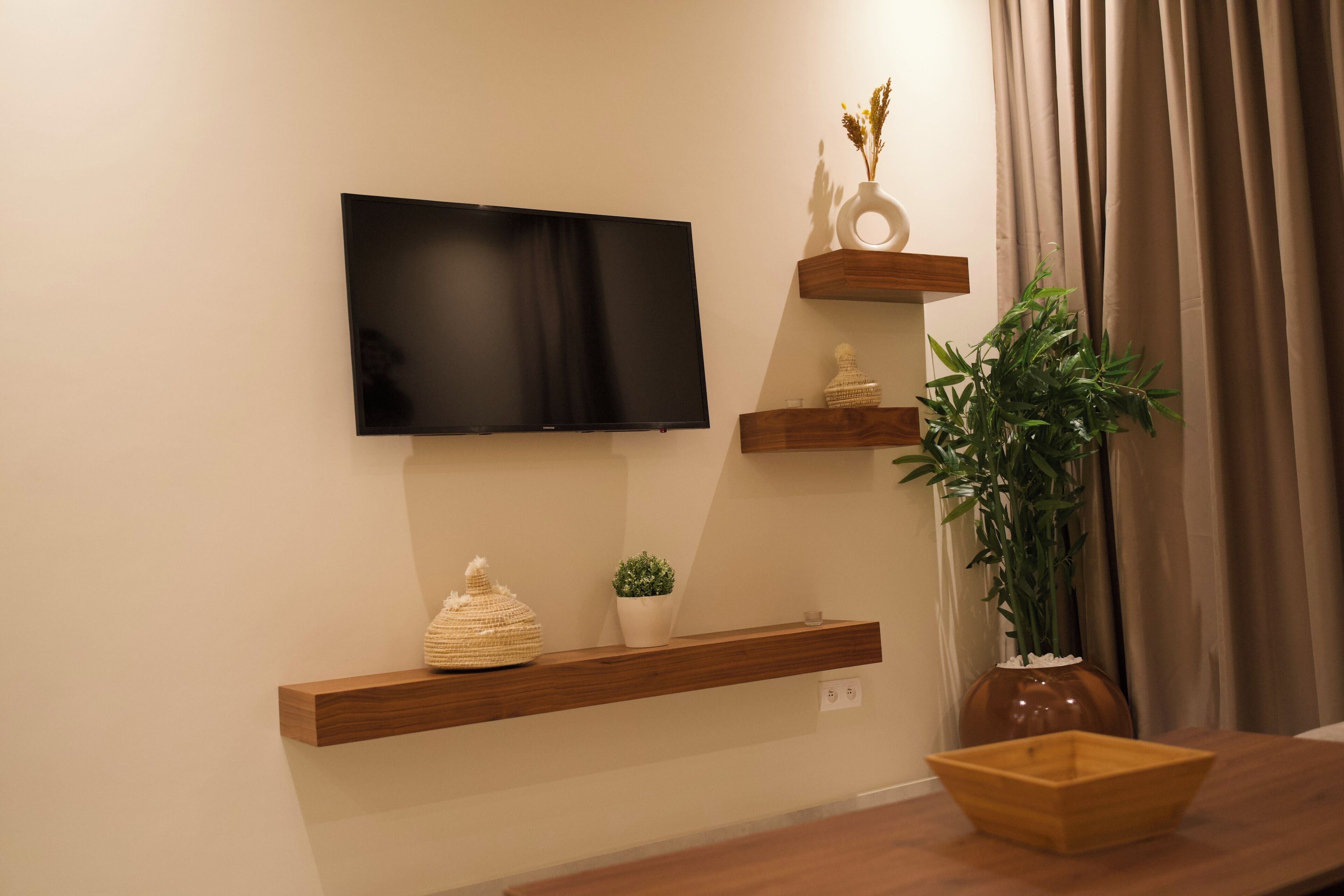 En moderne stue med et fladskærms-tv på væggen, træhylder med pyngegenstande, en potteplante og et træsidebord.