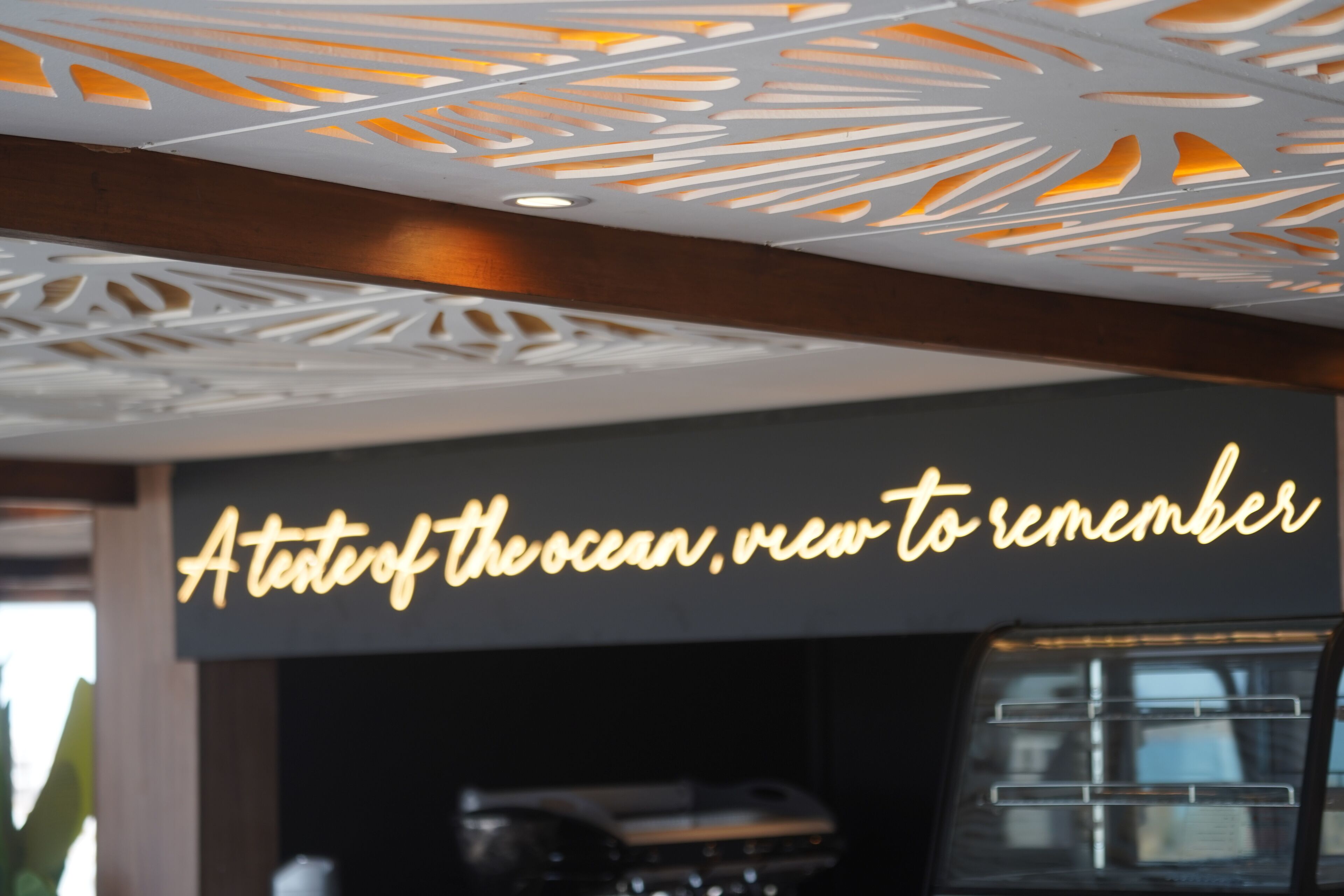 A ceiling with a geometric pattern and a sign that reads "A taste of the ocean, new to remember."