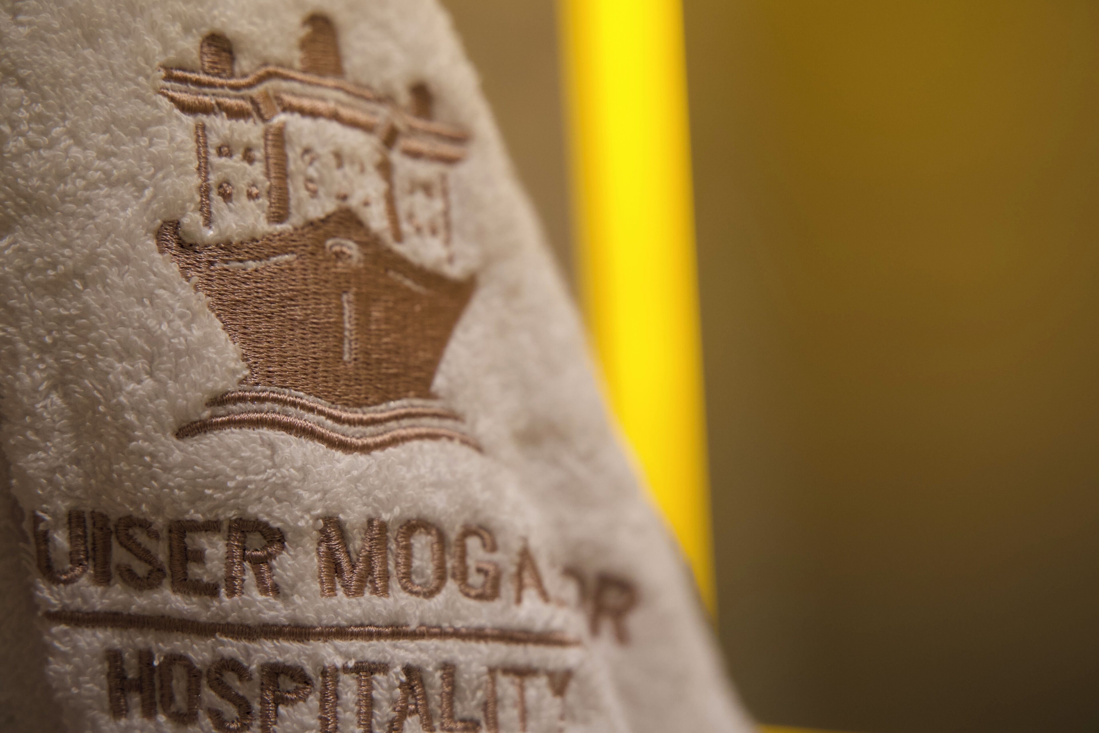 Ein Nahaufnahme eines Handtuchs mit eingesticktem Text und einem Gebäudedesign, vermutlich ein Hinweis auf ein Hotel oder einen Gastronomiebetrieb.