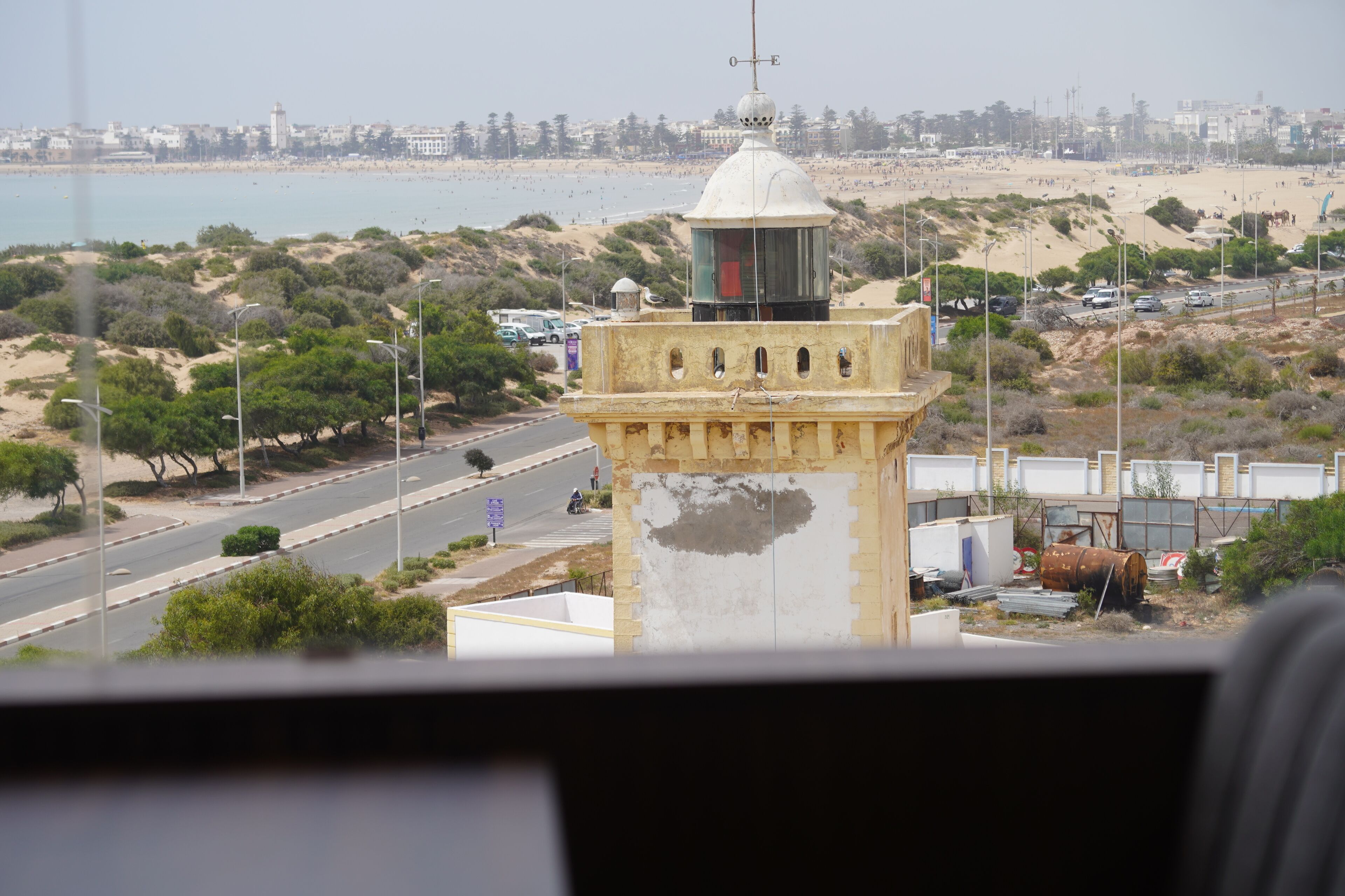 A coastal view with a lighthouse, beach, and urban area in the background.