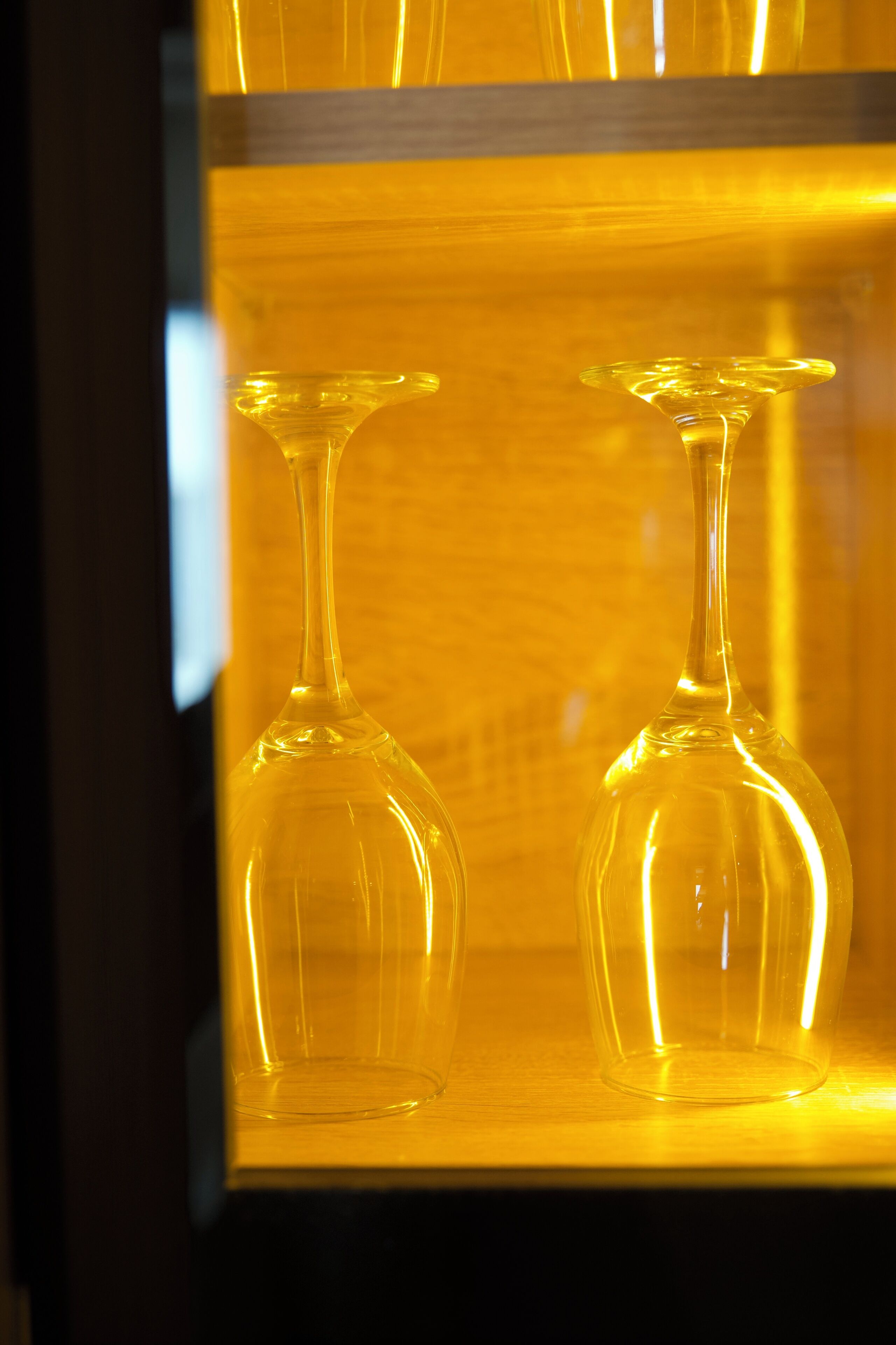 Two clear glass wine glasses in a yellow-lit display case.