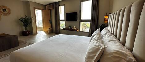 A spacious bedroom with a large bed, a television mounted on the wall, and a window with curtains.