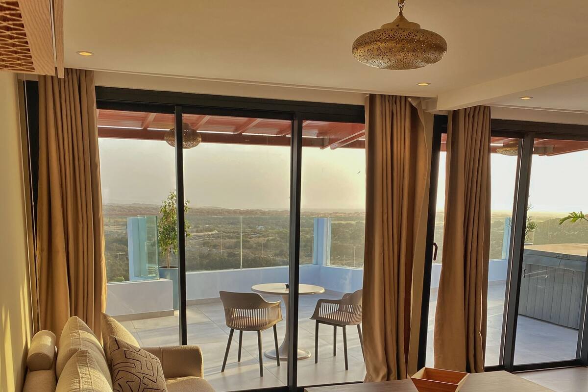 Een moderne woonkamer met een bank, een salontafel en uitzicht op een balkon met een tafel en stoelen.
