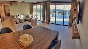 A modern living room with a sofa, a dining table, and a view of a cityscape through large windows. - Cruiser Mogador Hospitality (Essaouira)