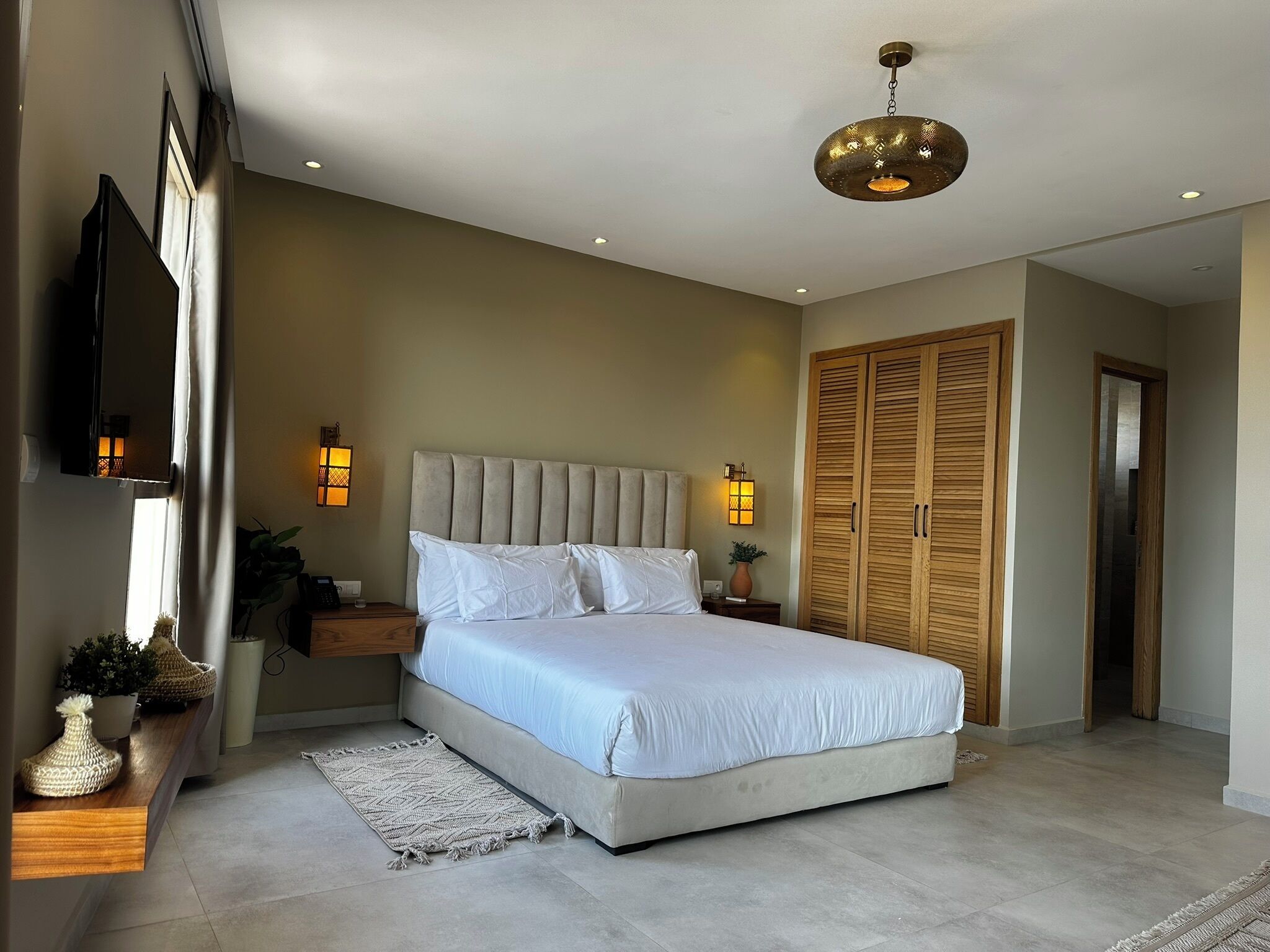 Quarto moderno com uma cama grande, luminárias de cabeceira, um guarda-roupa de madeira e um candeeiro de teto.