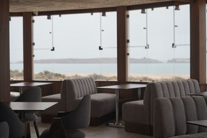 Un interior moderno con asientos y mesas dispuestas cerca de amplias ventanas con vista a una playa.