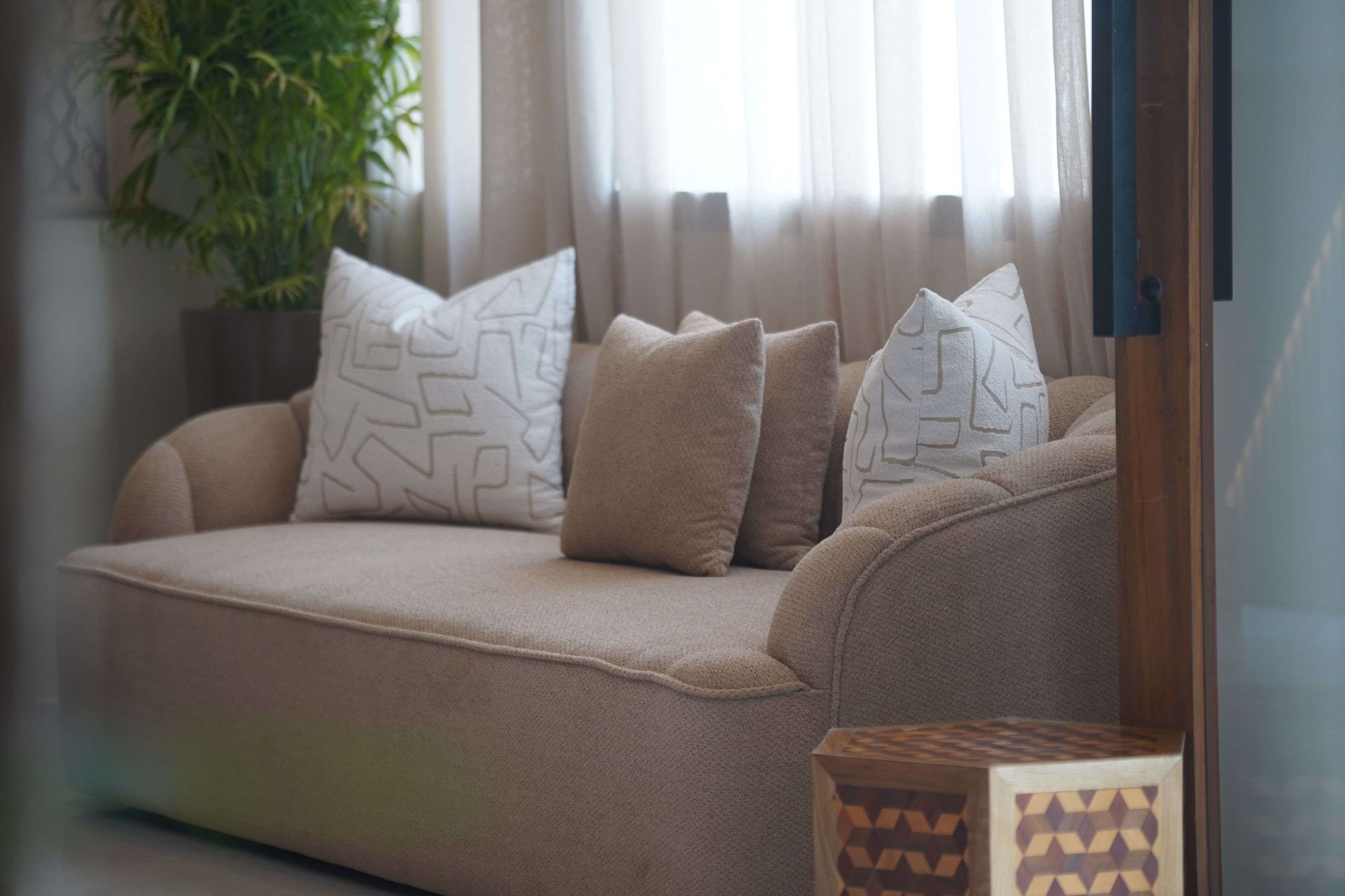 A beige sofa with patterned cushions, a wooden side table, and a potted plant in a modern living room.