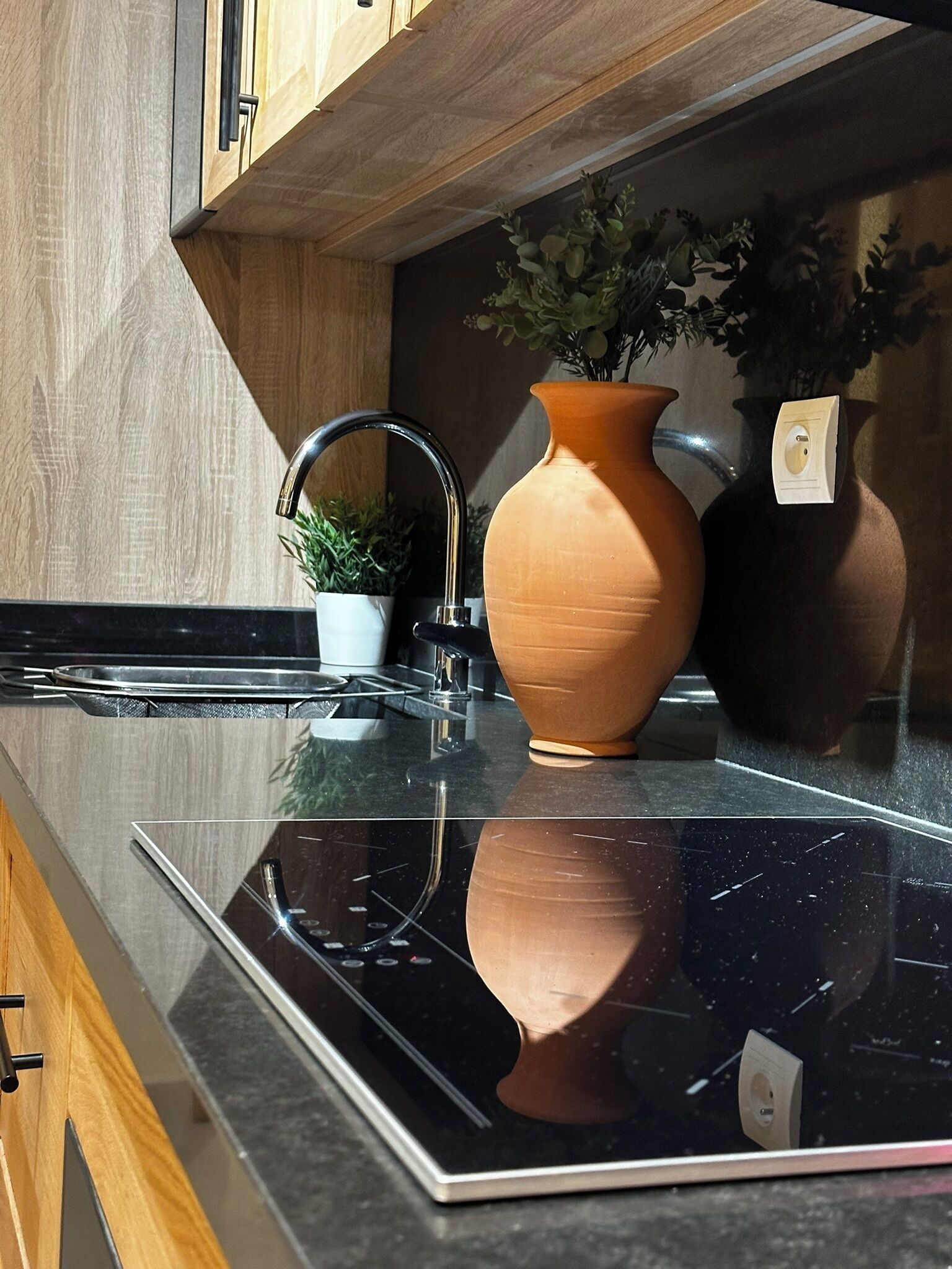 A kitchen with a black countertop, a white pot with a plant, a terracotta vase, and a modern faucet.