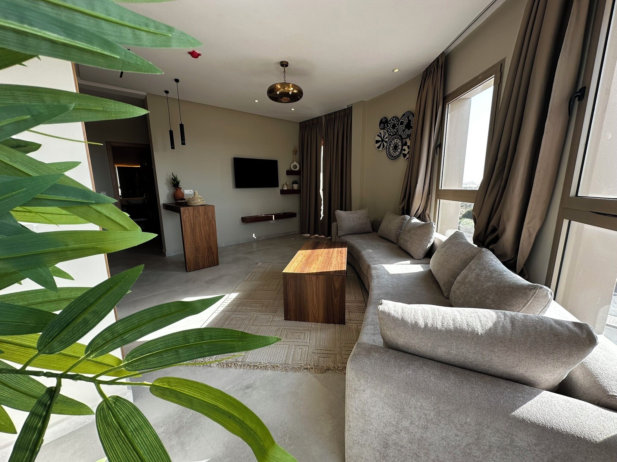 A modern living room with a large sofa, a wooden coffee table, and a TV mounted on the wall.
