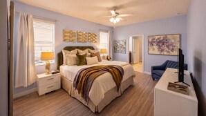 A bedroom with a bed, nightstands, a desk, a chair, a ceiling fan, and artwork on the walls. - The Magic Kingdom 9BR Resort Pool Home Near Disney (Four Corners)