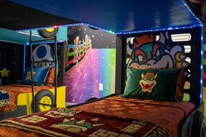 Une chambre avec un lit agrémenté d’un oreiller à l’effigie d’un personnage de dessin animé, un mur orné d’une fresque colorée et un plafond doté de lumières LED bleues.