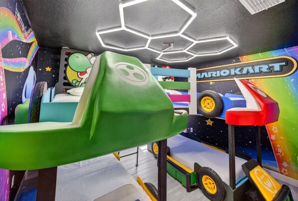 Un espace de jeux sur le thème de Mario Kart, avec une piste verte, des murs colorés et un plafond doté de luminaires hexagonaux.