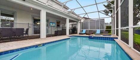 A swimming pool with a covered patio area, outdoor seating, and a view of the surrounding landscape.