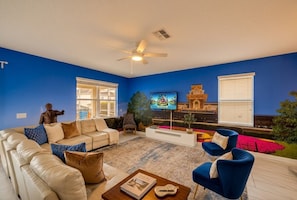 A living room with a beige sofa, blue armchairs, a coffee table, a TV, and a ceiling fan.