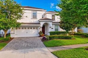 A two-story house with a garage, a driveway, and well-maintained landscaping. - The Magic Kingdom 9BR Resort Pool Home Near Disney (Four Corners)