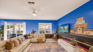 Ein Wohnzimmer mit einem Ecksofa, einem Couchtisch, einem Fernseher und einer Wandmalerei.
