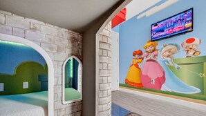 Ein Kinderspielbereich mit Mauerwerkdesign, einem an der Wand montierten Fernseher und einem Wandgemälde mit Zeichentrickfiguren.