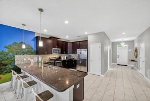 A modern kitchen with a large island, bar stools, and a view of the outdoors. - The Magic Kingdom 9BR Resort Pool Home Near Disney (Four Corners)