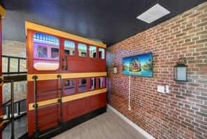 Ein Zimmer mit Backsteinwand, einem Wandgemälde, einem Fernseher und einer bussähnlichen Holzkonstruktion.