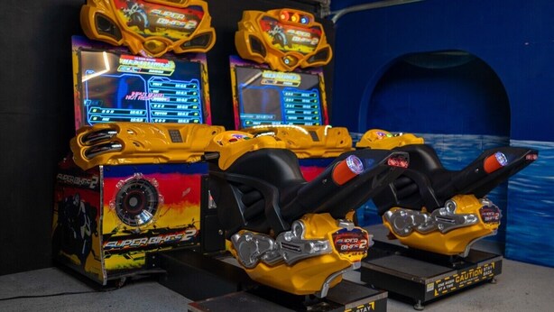 Eine Reihe von Spielautomaten mit Rennspielen vor einer blauen Wand.