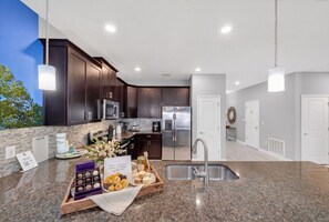 A modern kitchen with dark cabinets, stainless steel appliances, granite countertops, and a sink. - The Magic Kingdom 9BR Resort Pool Home Near Disney (Four Corners)