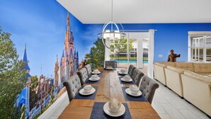 A dining area with a long table set for six, a mural of a castle on the wall, and a statue in the corner. - The Magic Kingdom 9BR Resort Pool Home Near Disney (Four Corners)