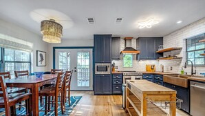 A modern kitchen with dark cabinets, a wooden dining table, and a built-in oven. - Hilltop Oasis w/Pool, Hot Tub, Fire Pit + Views (Dripping Springs)