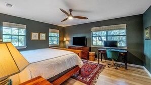 A bedroom with a bed, desk, TV, and windows. - Hilltop Oasis w/Pool, Hot Tub, Fire Pit + Views (Dripping Springs)