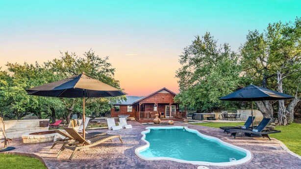 A backyard with a swimming pool, lounge chairs, and umbrellas. - Hilltop Oasis w/Pool, Hot Tub, Fire Pit + Views (Dripping Springs)