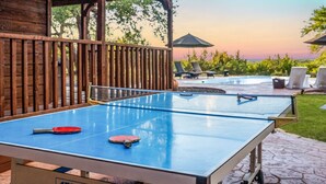 A ping pong table with two paddles, a covered seating area, and lounge chairs. - Hilltop Oasis w/Pool, Hot Tub, Fire Pit + Views (Dripping Springs)