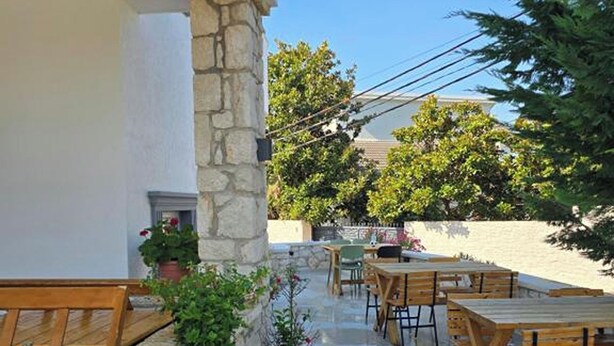 An outdoor patio with stone walls, wooden tables, and chairs. - Vila Anhel (Ksamil)