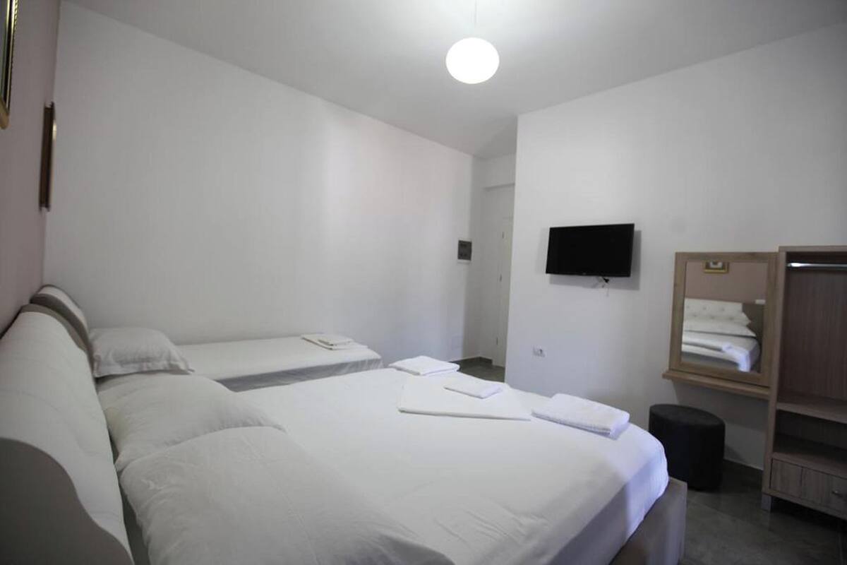 A hotel room with two single beds, a flat-screen TV mounted on the wall, a wooden wardrobe, and a small stool.