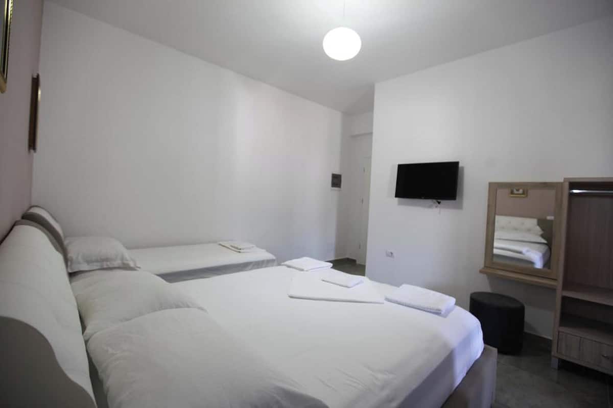 A hotel room with two single beds, a flat-screen TV mounted on the wall, a wooden wardrobe, and a small stool.