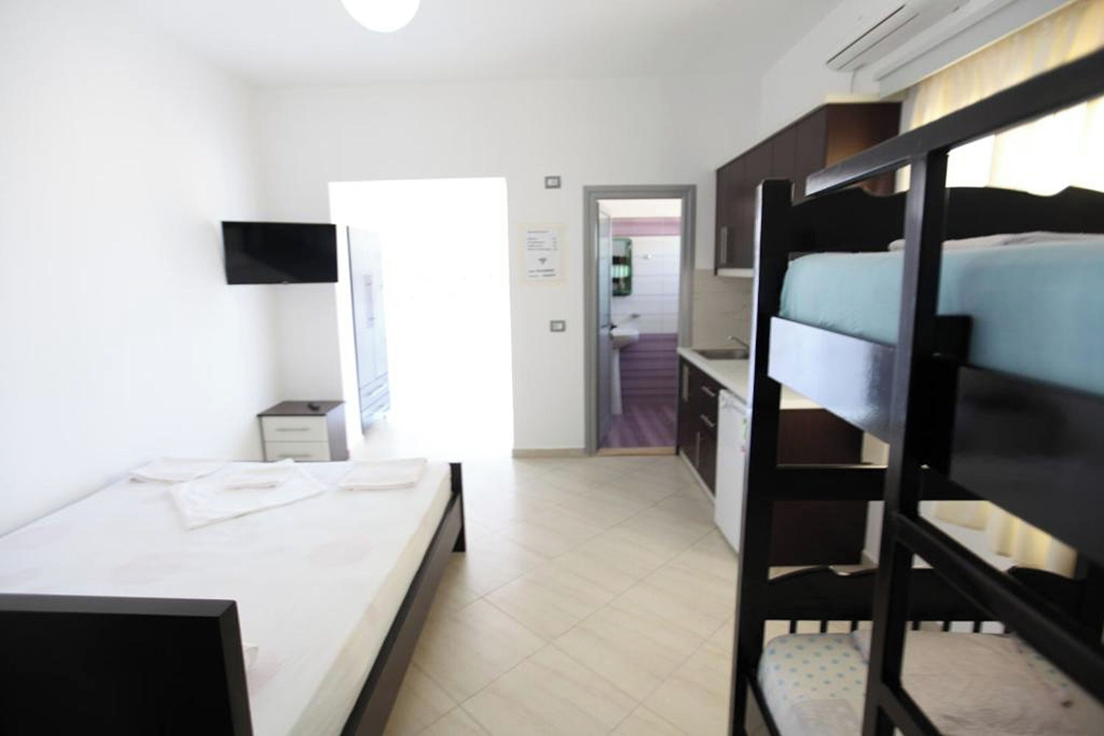 A hotel room with a bunk bed, a single bed, a desk, a chair, and a TV mounted on the wall.