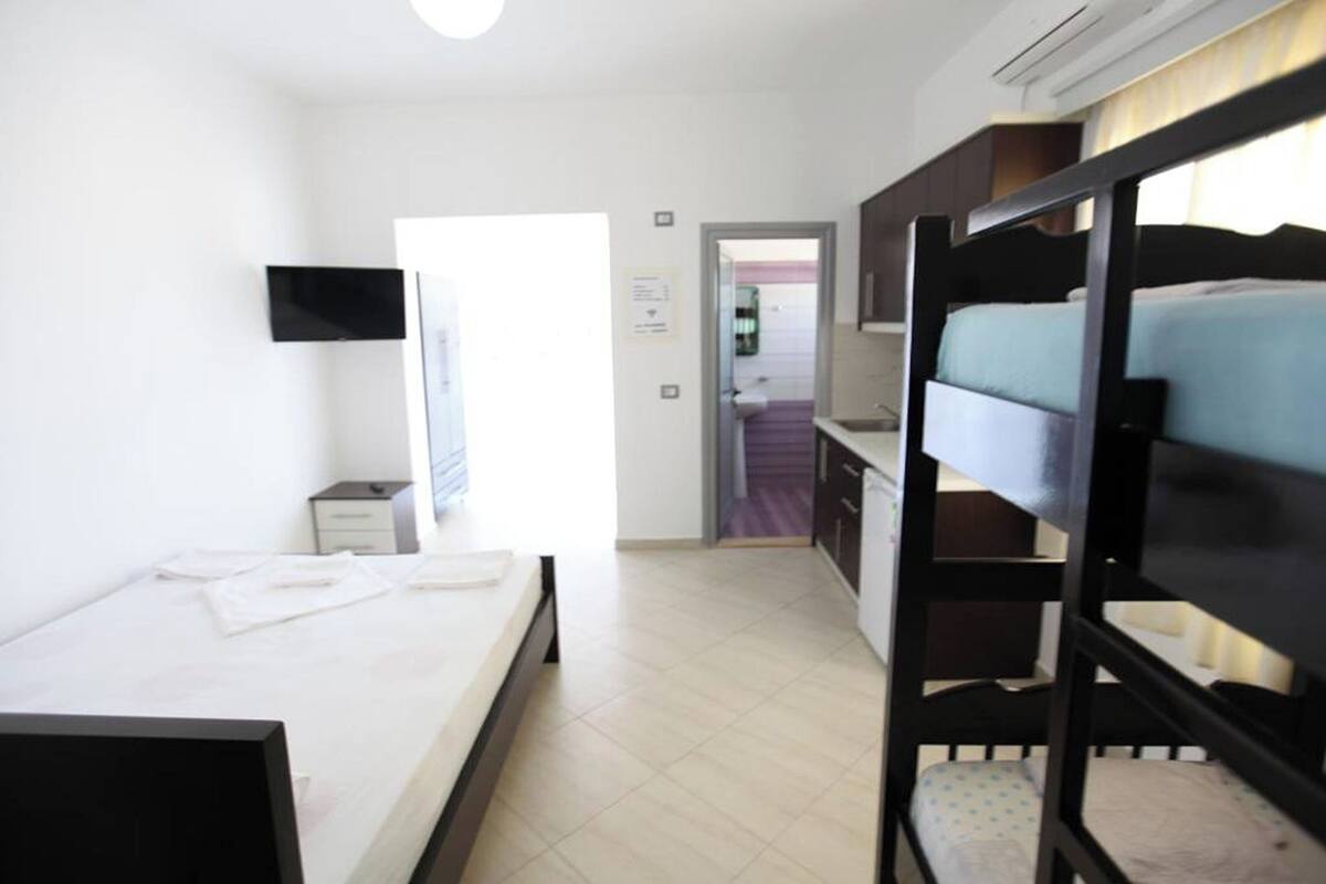 A hotel room with a bunk bed, a single bed, a desk, a chair, and a TV mounted on the wall.