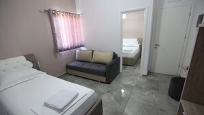 A hotel room with a bed, a sofa, and a door leading to another room. - Vila Anhel (Ksamil)