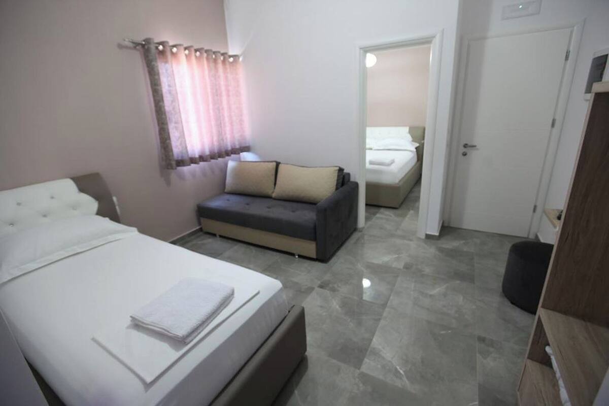 A hotel room with a bed, a sofa, and a door leading to another room.