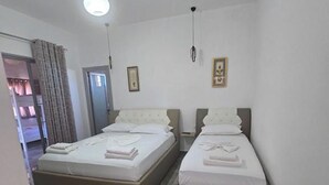A hotel room with two beds, a door, and a ceiling light. - Vila Anhel (Ksamil)
