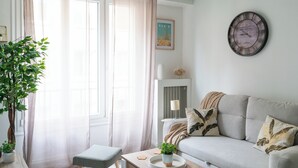 En stue med sofa, et lille bord med en plante, en stol og et vægur.
