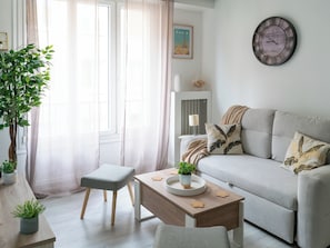Ein Wohnzimmer mit einer Couch, einem kleinen Tisch mit Pflanze, einem Sessel und einer Wanduhr.
