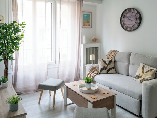 A living room with a sofa, a small table with a plant, a chair, and a wall clock.