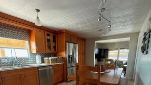 Una cocina con armarios de madera, un refrigerador de acero inoxidable, un fregadero y una zona de comedor con mesa y sillas de madera.