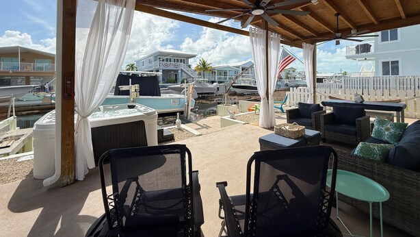 Un patio al aire libre con mobiliario de mimbre, un ventilador de techo y vistas a barcos y casas.