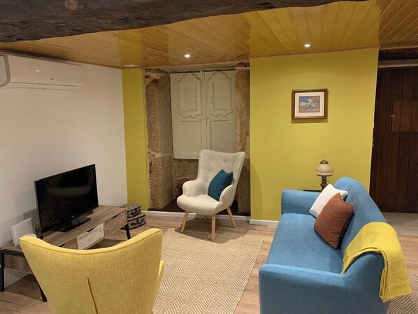 A living room with a TV, a yellow armchair, a blue sofa, and a white armchair. - Casarupa do Viriato (Torre de Moncorvo)